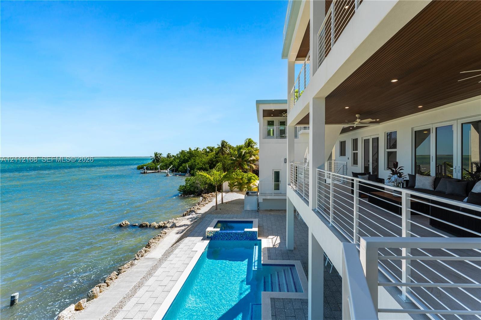 Multi-level waterfront residence featuring a lap pool with an integrated spa, expansive covered balcony with slatted wood-finish ceilings, metal raili