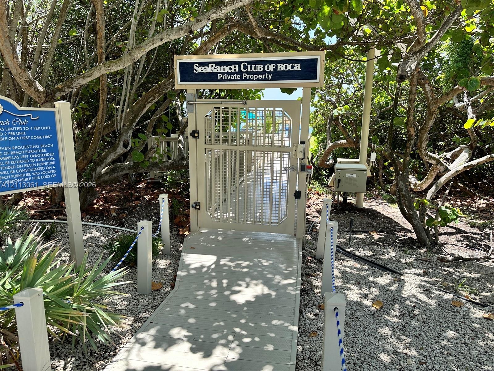 Secured entry gate with access control system, elevated walkway, and roped pathway markers surrounded by mature native landscaping