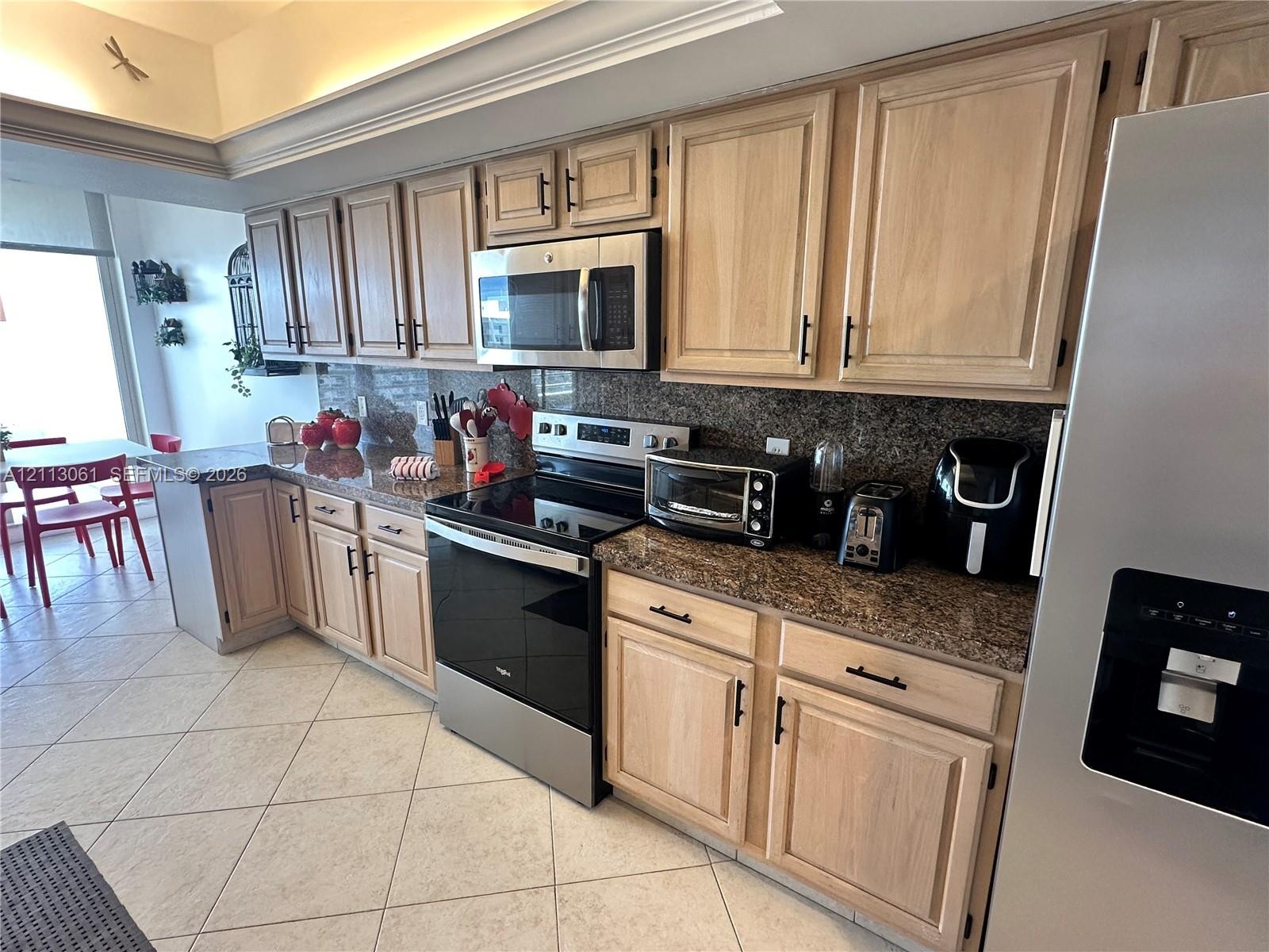 Kitchen featuring light-finish cabinetry, stone-surface countertops, tile flooring, and stainless steel appliances