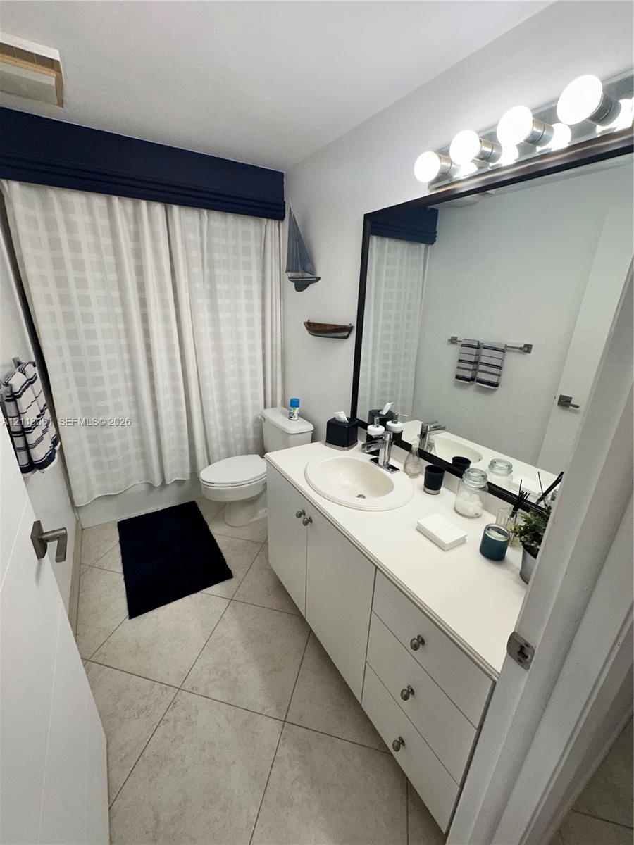 Bathroom featuring a vanity with a white countertop and oval undermount sink, large wall-mounted mirror, multi-bulb light fixture, and stone-finish fl