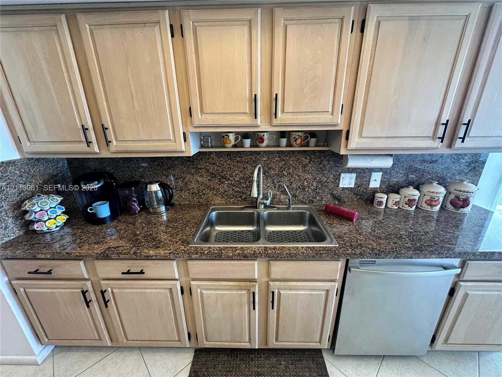 Light-toned wood cabinetry with matte black hardware, stone-finish countertops, dual-basin stainless steel sink, pull-down faucet, and integrated stai