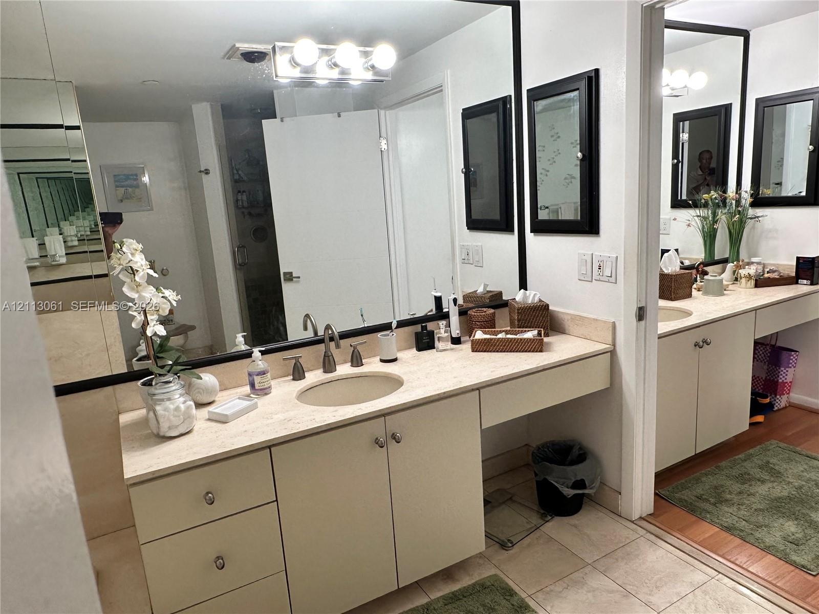 Bathroom featuring a dual-vanity setup with stone countertops, undermount sinks, wall-to-wall mirrors, and built-in cabinetry with metallic hardware