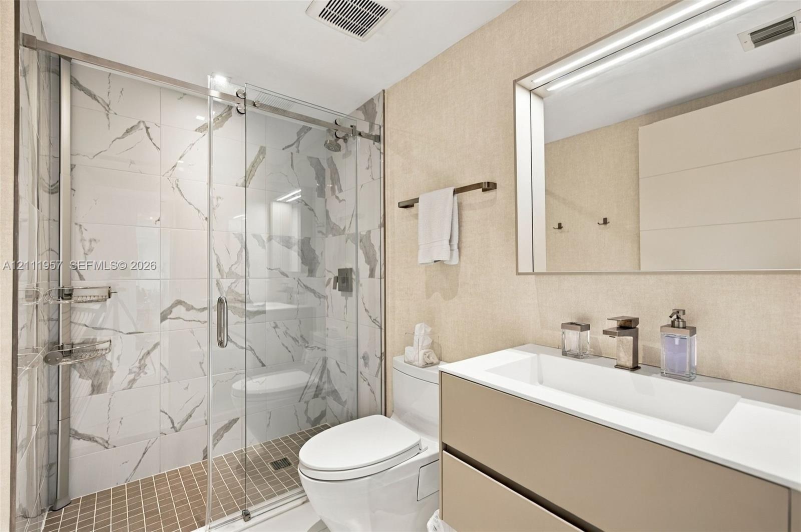 Floating vanity with integrated rectangular sink and metallic faucet, complemented by a walk-in shower featuring sliding glass doors and large-format 