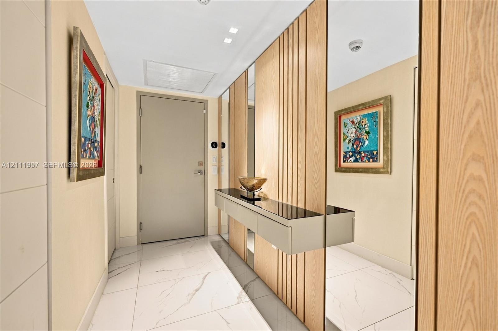 Entryway featuring large-format white tile flooring, vertical wood slat wall paneling, floor-to-ceiling mirror accents, and a built-in wall-mounted co