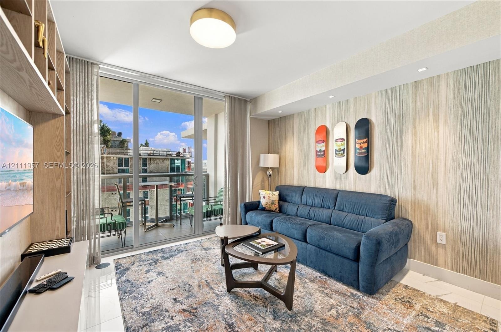 Living area featuring floor-to-ceiling glass sliding doors, built-in open-shelf cabinetry, textured accent wall, polished tile flooring, and flush-mou