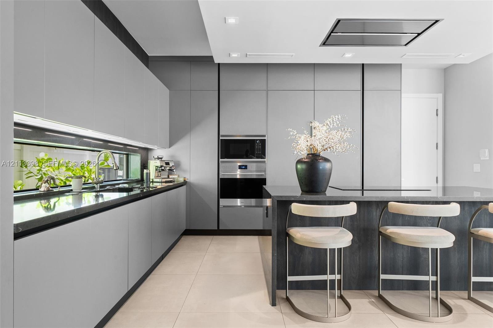 Modern kitchen featuring matte grey flat-panel cabinetry, dark stone countertops, built-in stainless steel appliances, a horizontal window backsplash,