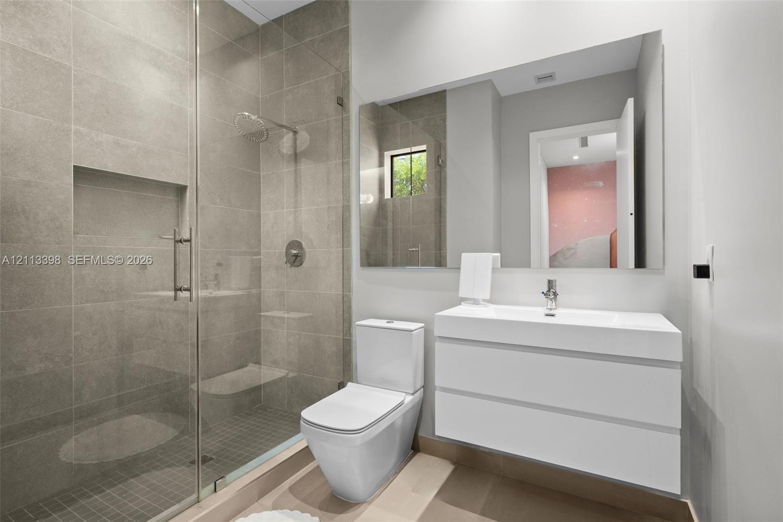 Modern bathroom featuring a glass-enclosed shower with tiled walls and a built-in recessed niche, a white floating vanity with a seamless integrated s