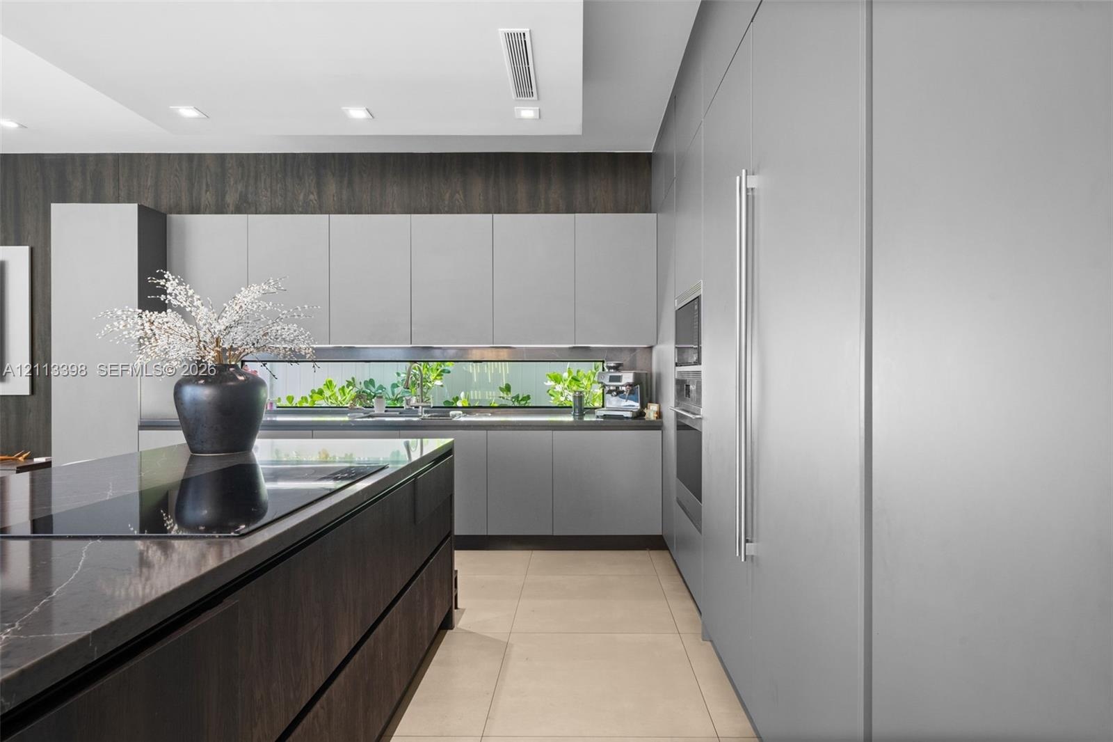 Contemporary kitchen featuring flat-panel cabinetry, a dark-toned center island with a stone-surface countertop, integrated stainless steel appliances