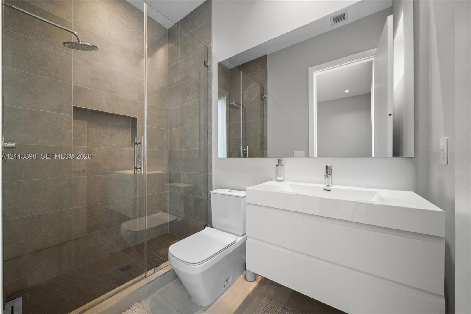 Walk-in shower with floor-to-ceiling tile, rainfall showerhead, and glass enclosure, featuring a white floating vanity with an integrated basin and a 
