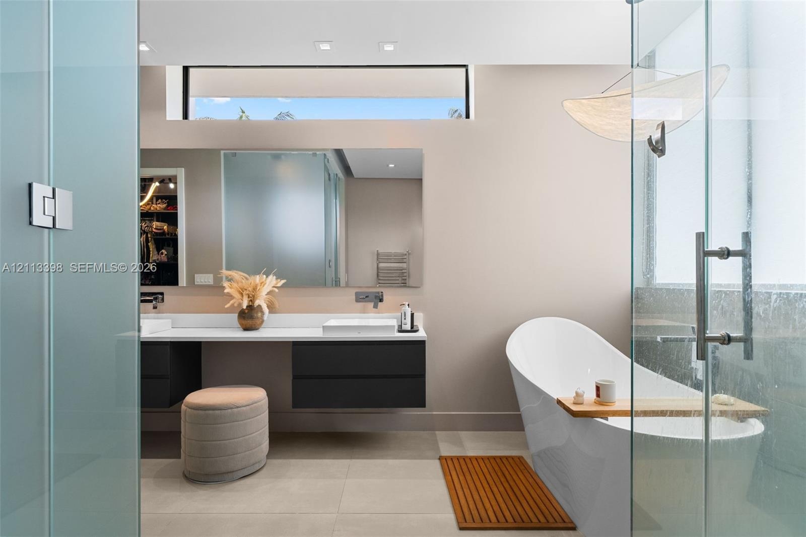 Floating dual-vanity with matte cabinetry and solid-surface countertop, freestanding soaking tub, frameless glass-enclosed shower, clerestory window, 