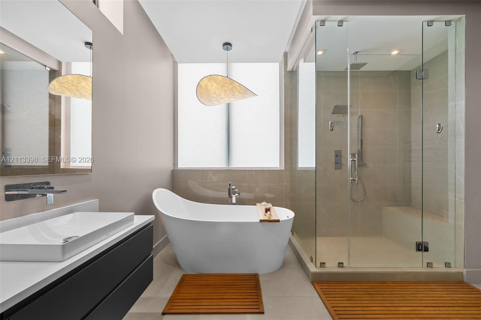 Modern floating vanity with a vessel sink and wall-mounted faucet, freestanding soaking tub, glass-enclosed walk-in shower with a built-in bench, and 