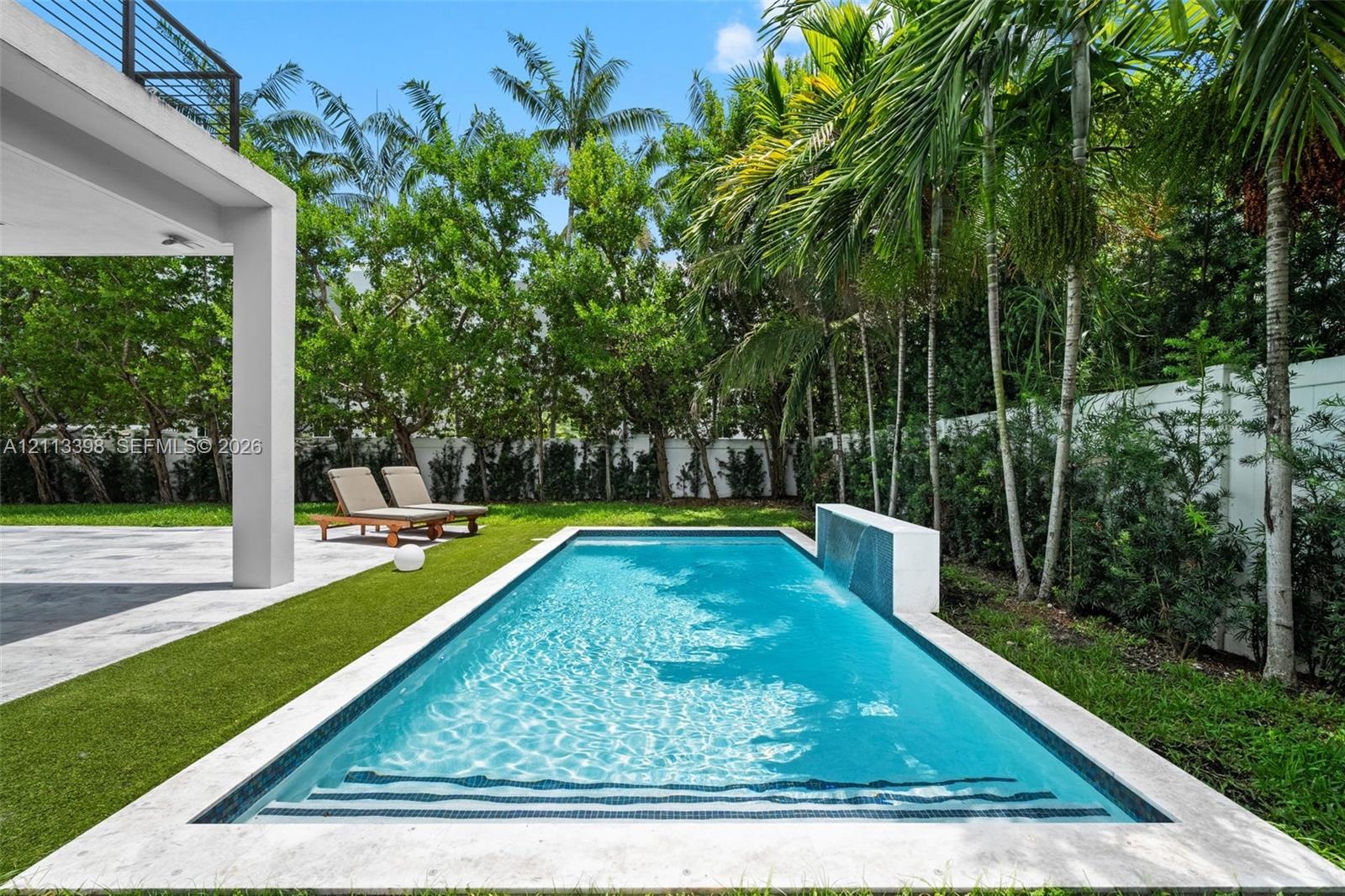 Rectangular swimming pool featuring a tiled water feature, stone paver coping, and artificial turf surrounds