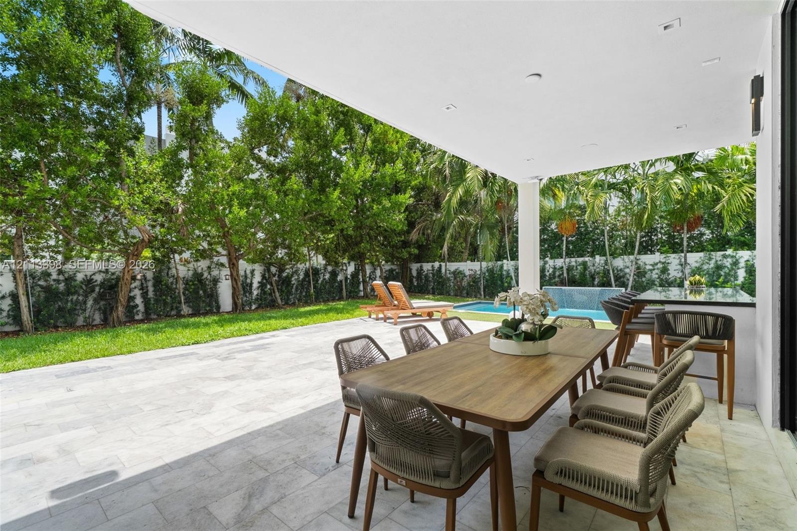 Covered outdoor patio featuring large-format stone tiling, integrated recessed lighting, a built-in outdoor bar with countertop, an in-ground swimming
