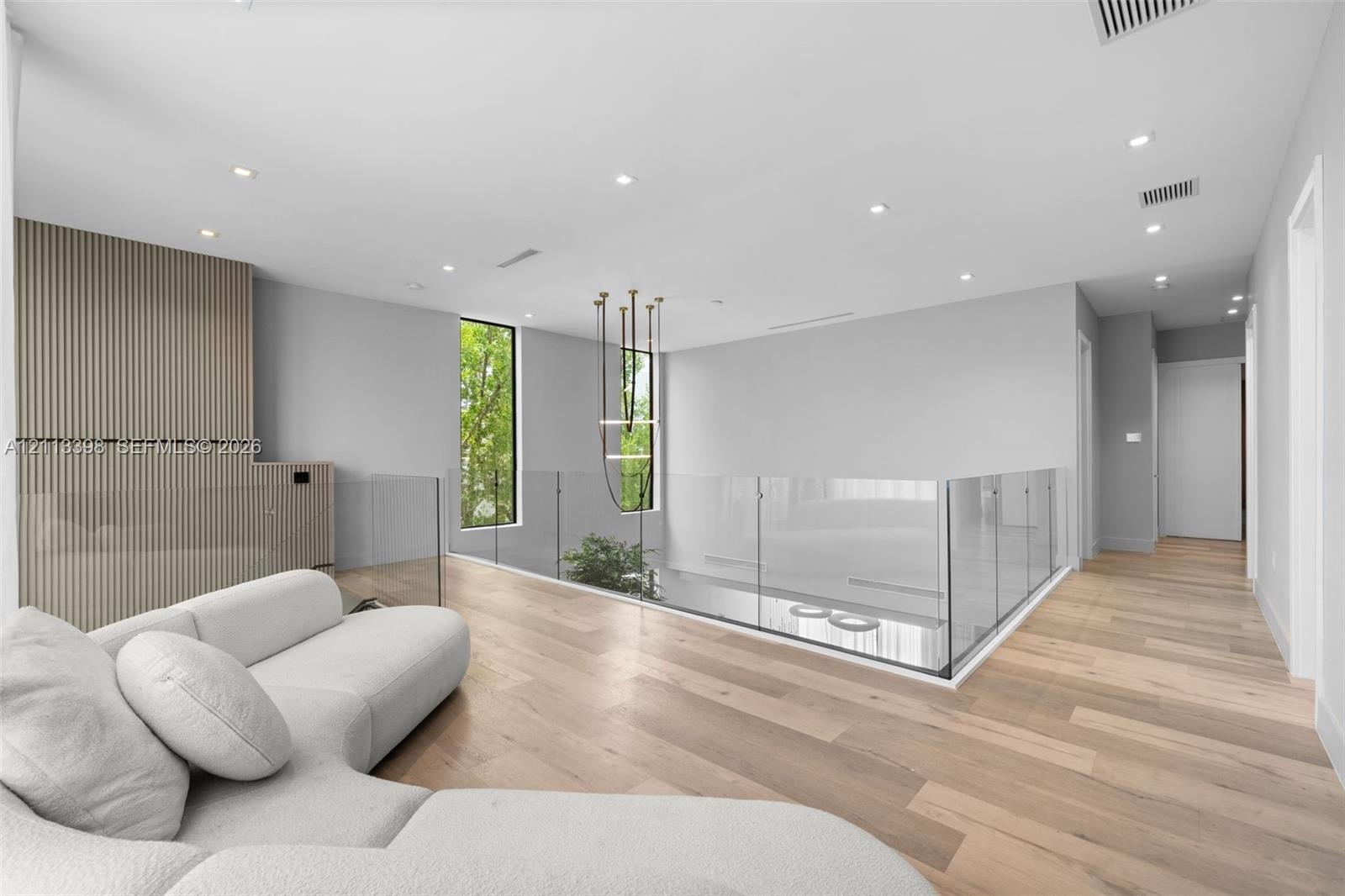 Open-concept space featuring wood-finish flooring, a glass panel railing, vertical wood-slat wall paneling, recessed lighting, and a modern tiered cha