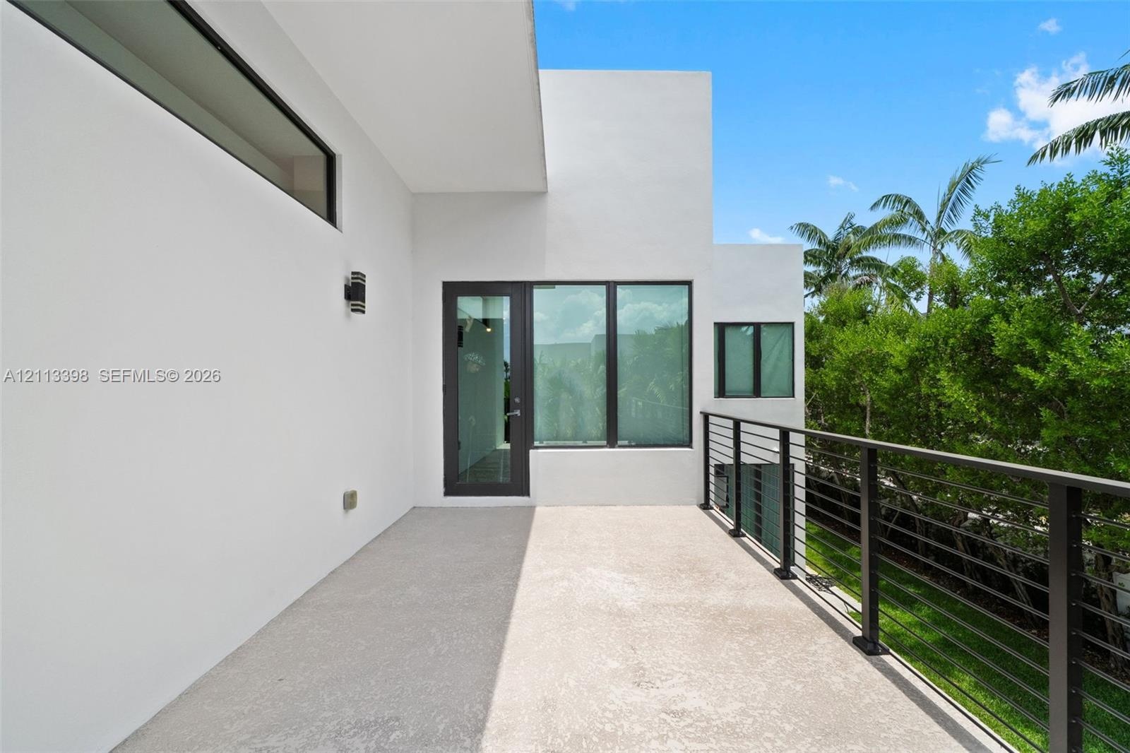 Covered exterior terrace featuring a smooth concrete floor, minimalist white stucco exterior walls, dark-framed expansive windows, and a metal horizon