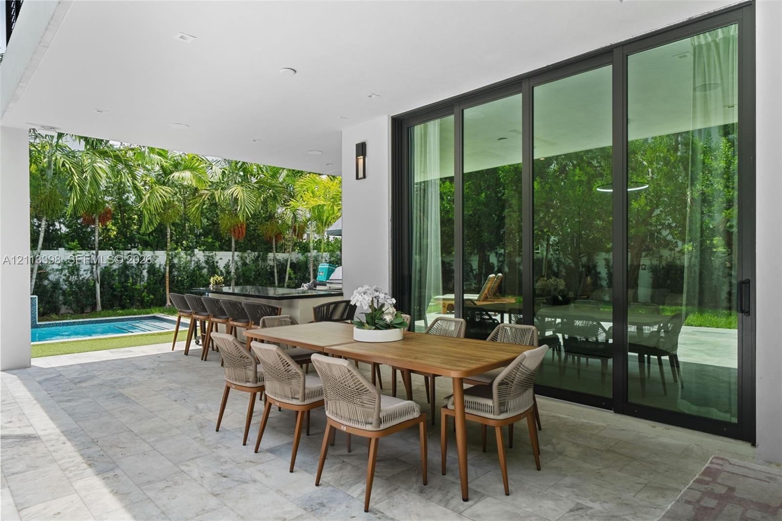 Covered patio featuring stone-tile flooring, floor-to-ceiling glass sliding doors, recessed lighting, and a built-in outdoor kitchen with a stone coun