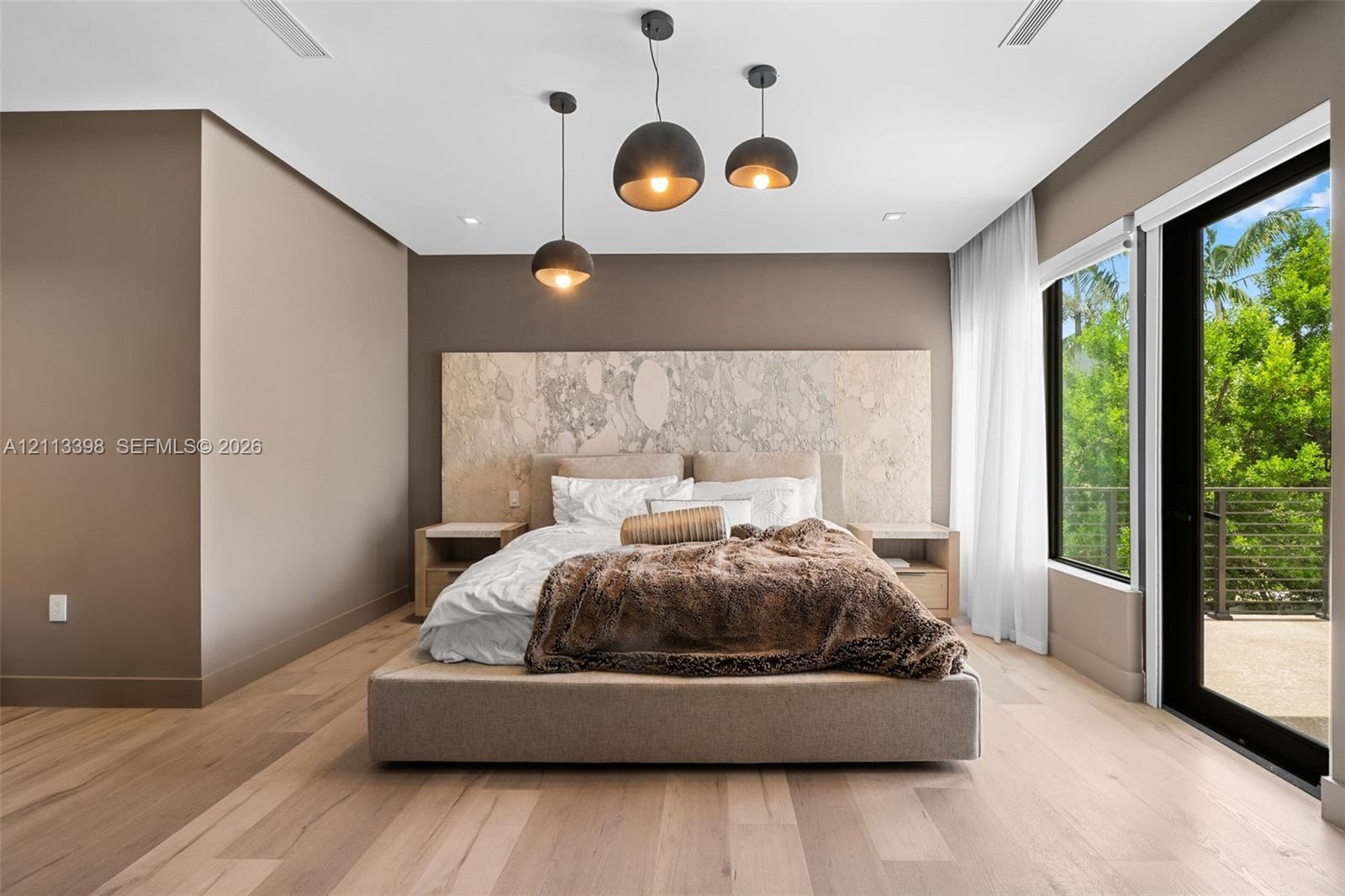 Custom full-height stone-textured headboard wall, light-toned wood-finish flooring, trio of suspended pendant lights, and floor-to-ceiling glass slidi