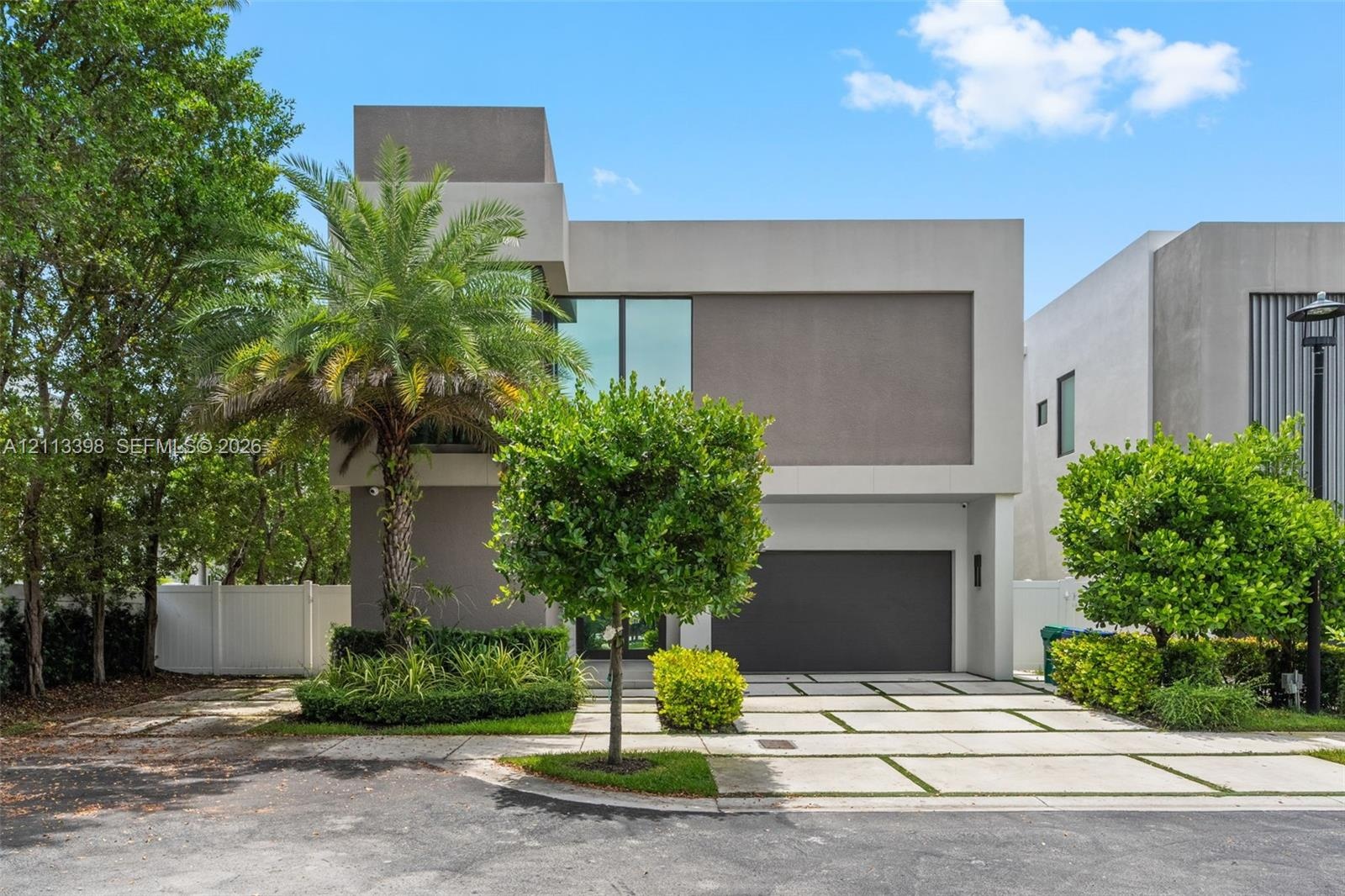 Contemporary two-story exterior featuring a smooth stucco facade, floor-to-ceiling windows, attached two-car garage, and a geometric concrete paver dr