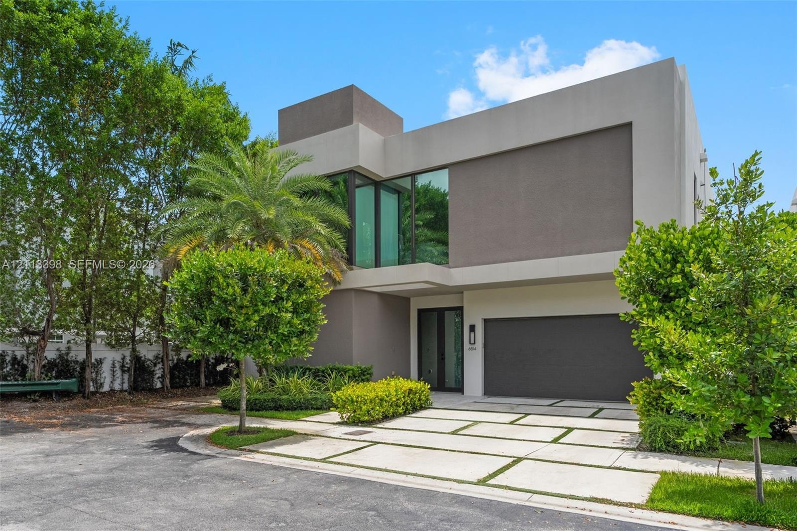 Modern multi-level exterior featuring smooth stucco facade, floor-to-ceiling glass windows, integrated covered entryway, and segmented concrete paver 