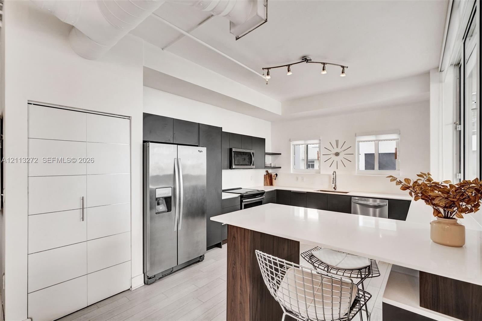 Kitchen featuring flat-panel cabinetry, quartz countertops, stainless steel appliances, track lighting, and wood-finish cabinetry on the island