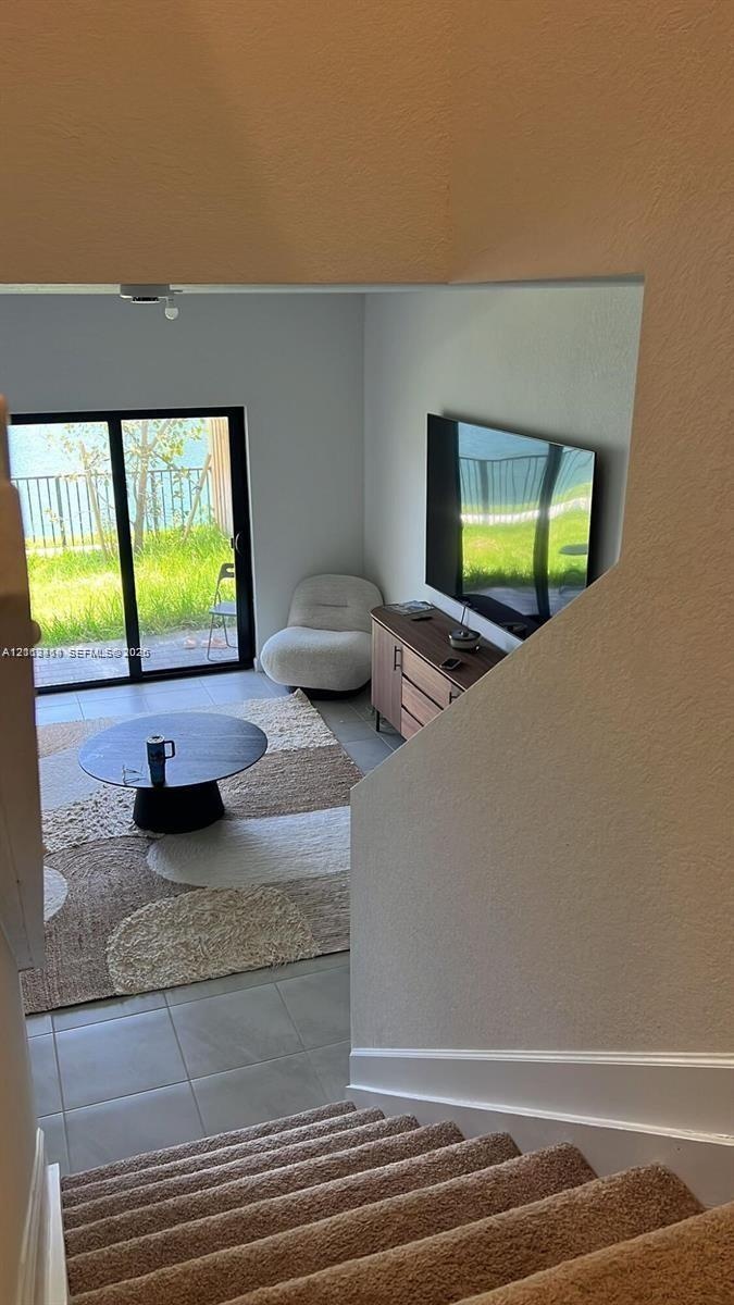 Interior space featuring neutral-toned carpeting on stairs, large-format tile flooring, and a sliding glass door providing external access