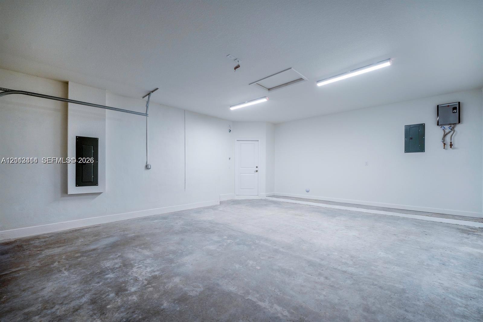 Finished garage featuring smooth walls, concrete flooring, dual overhead LED lighting fixtures, and an attic access panel