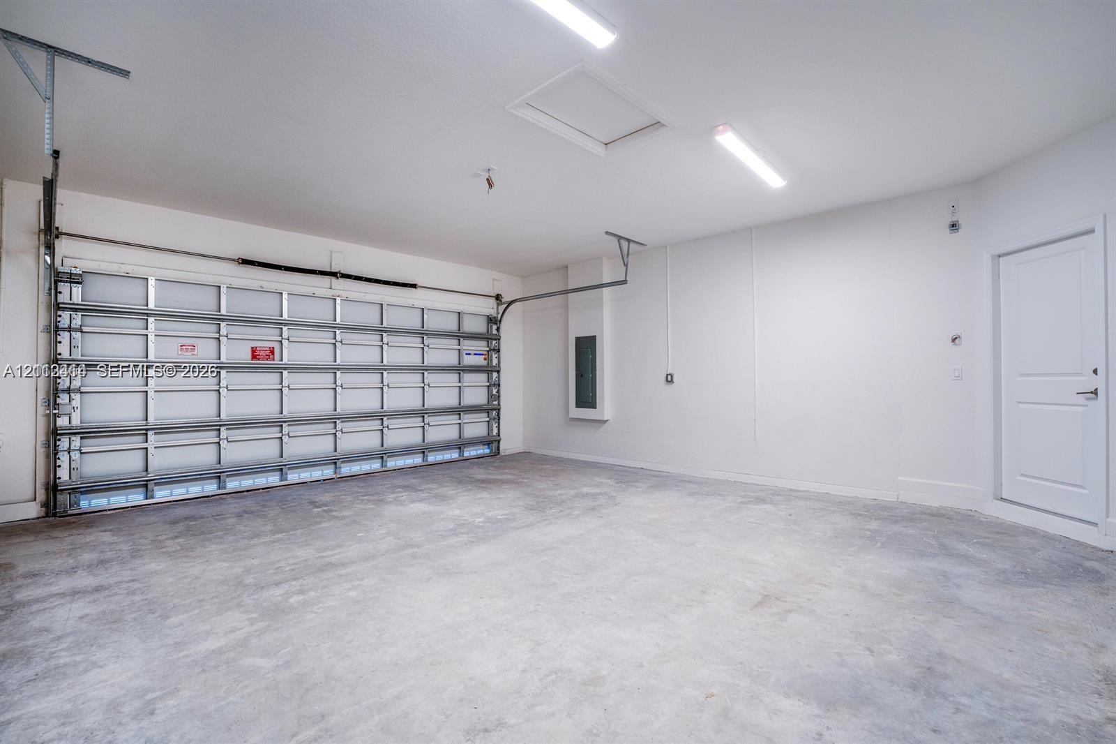 Garage interior featuring concrete flooring, LED strip lighting, an integrated electrical panel, and a paneled roll-up garage door