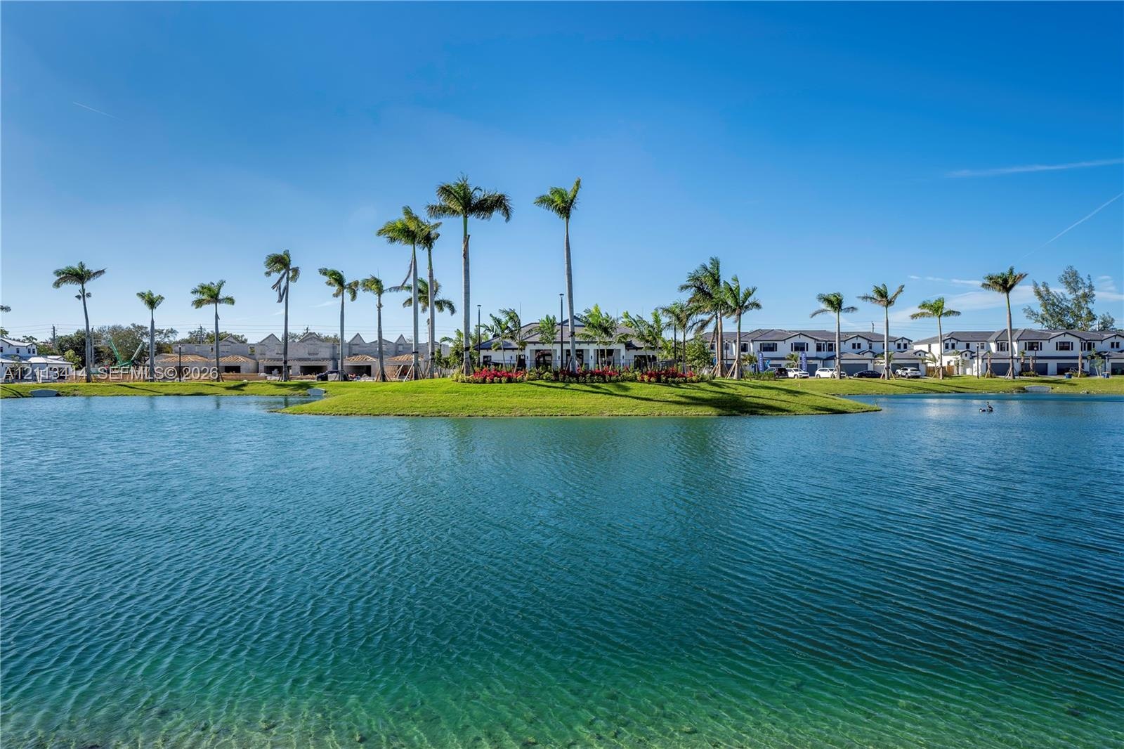 Expansive lakefront setting featuring a central island, manicured lawn, and mature palm trees