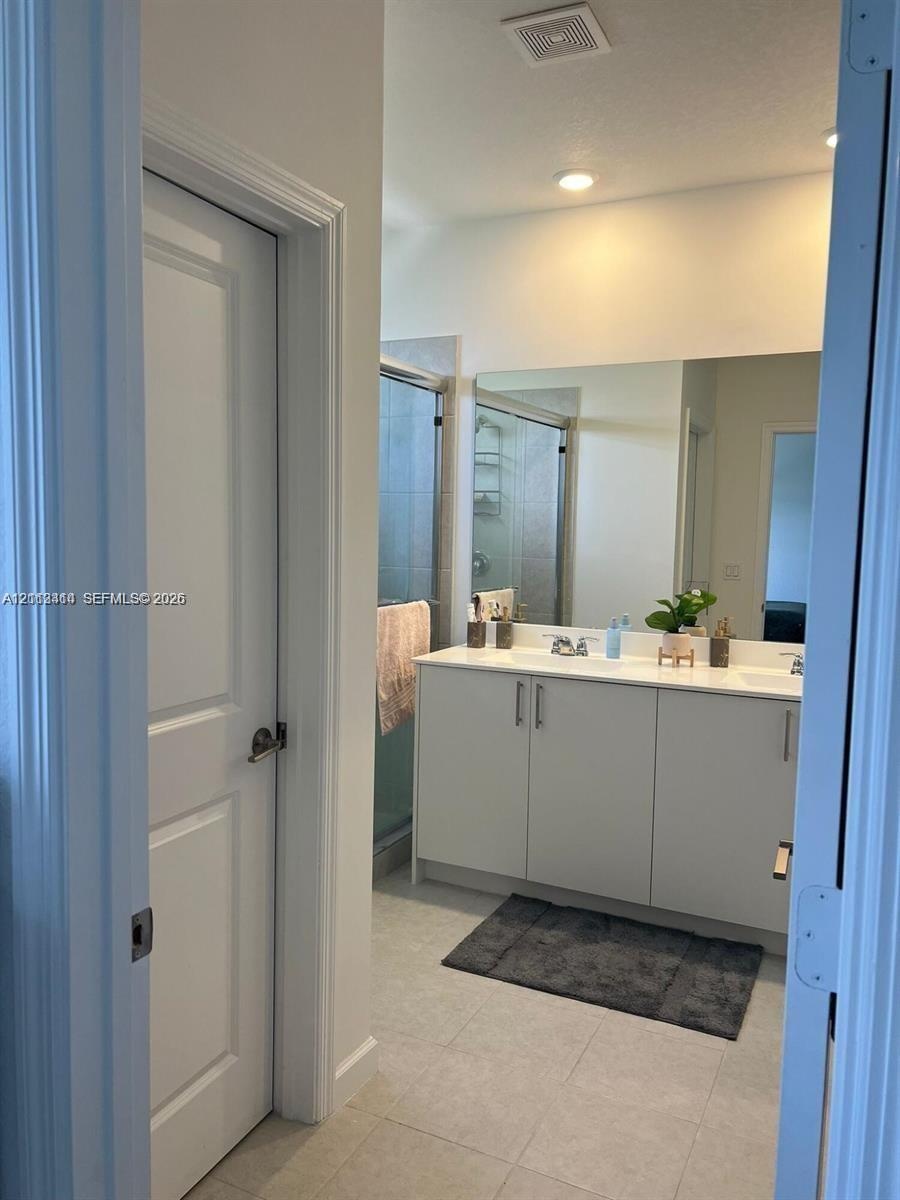 Dual-sink vanity with light-toned cabinetry, light-colored countertops, large wall-mounted mirror, and glass-enclosed shower featuring tile surrounds