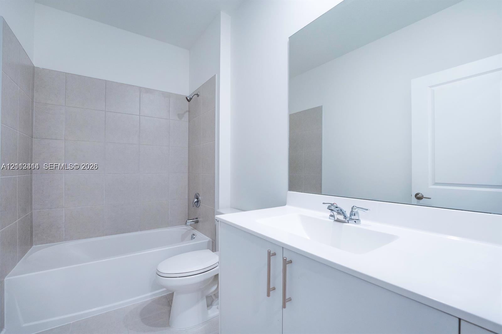 Bathroom featuring a white vanity cabinet with a solid surface countertop, an undermount sink with chrome fixtures, a full-width wall mirror, and a ti