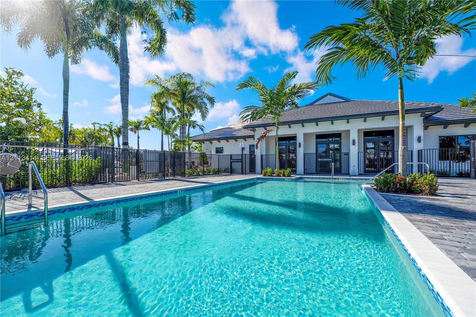 In-ground swimming pool with tile border, paver stone decking, and mature palm landscaping enclosed by metal fencing