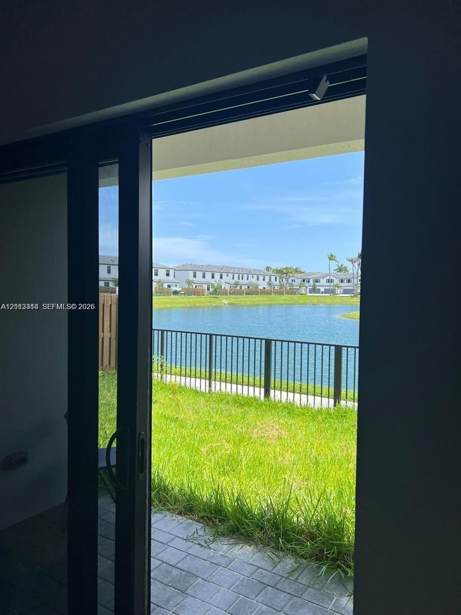 Black-framed sliding glass door opening to a paved patio, metal perimeter fencing, and waterfront scenery