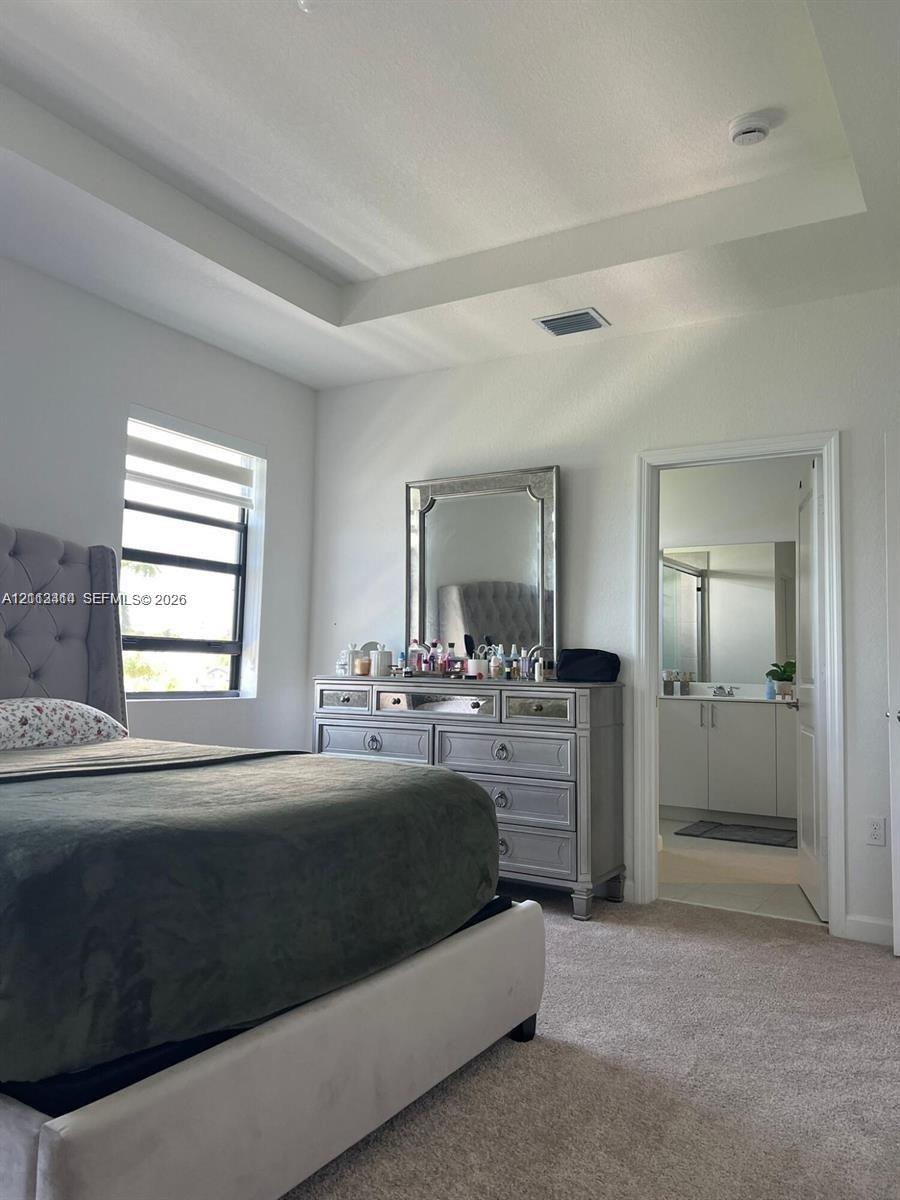 Tray ceiling, neutral carpeting, and window with horizontal blinds