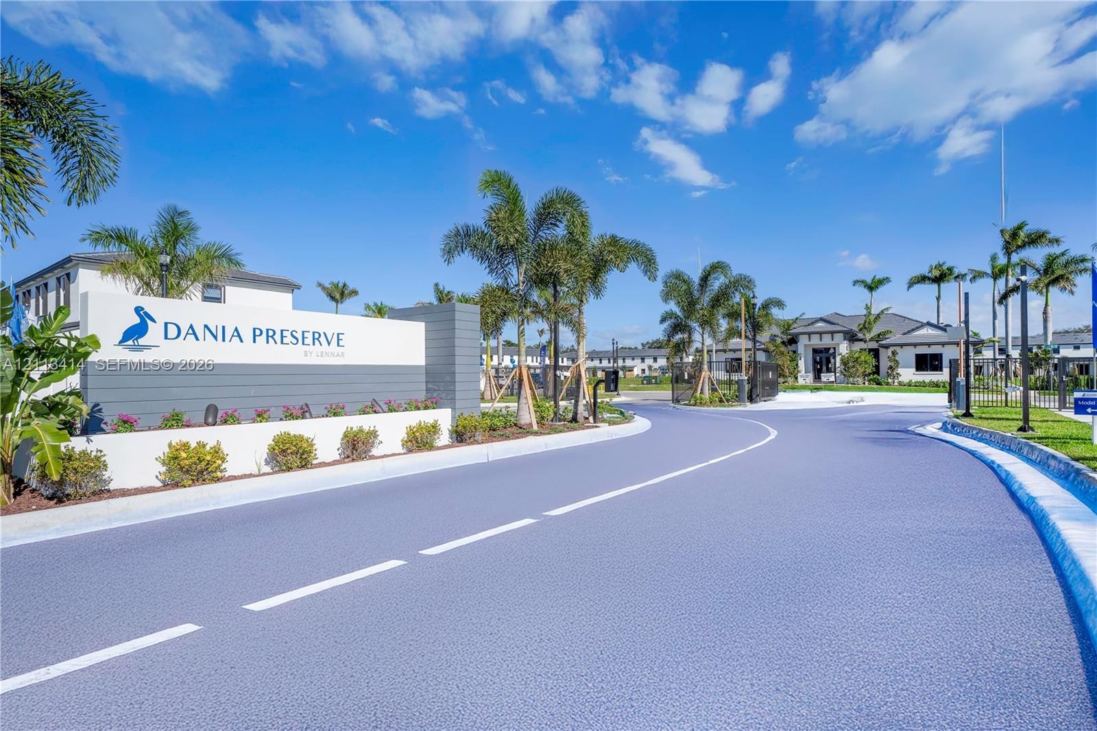 Community entrance featuring a branded masonry monument sign, mature palm landscaping, paved roadways, and gated access