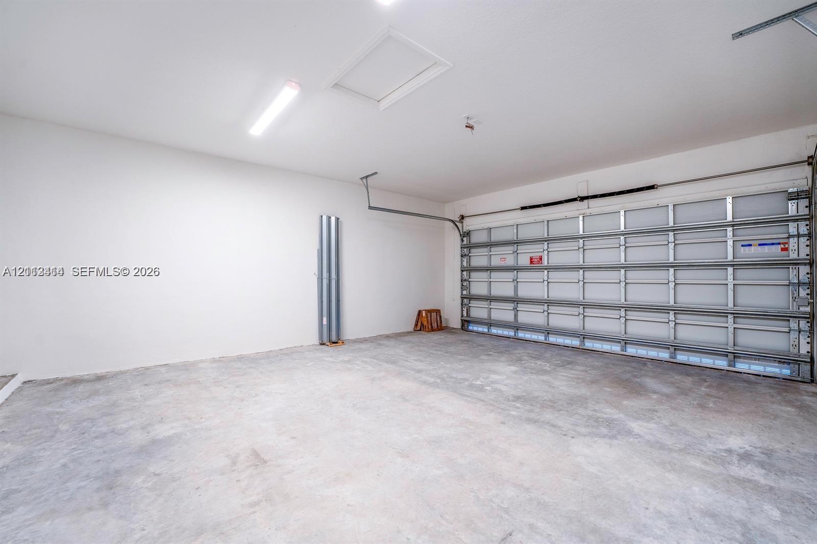 Finished garage featuring smooth-finish walls, exposed panel-style garage door, concrete flooring, and overhead lighting