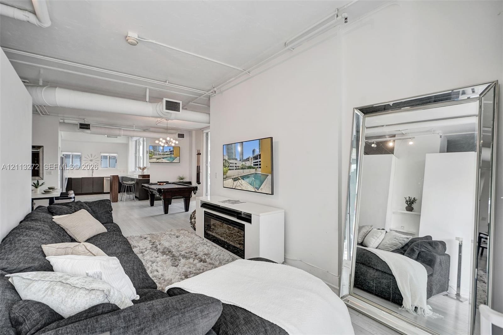 Open-concept interior featuring industrial-style exposed ductwork, white painted brick walls, wood-finish flooring, and a built-in wall-mounted electr