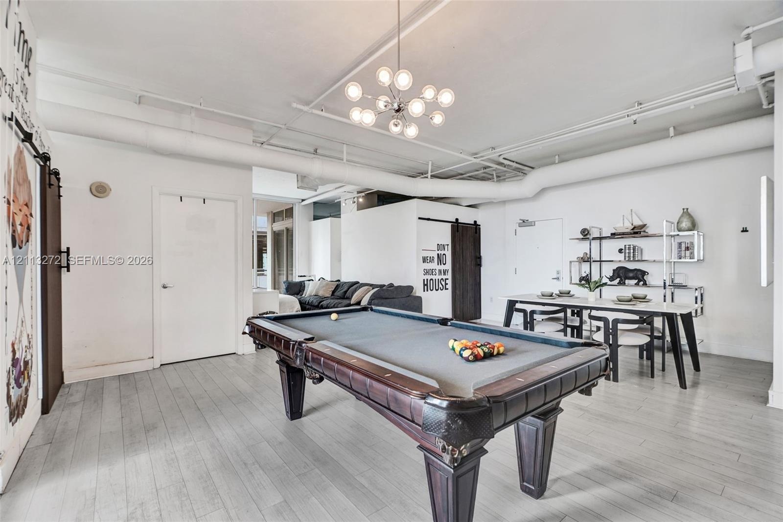 Open-concept industrial-style interior featuring high ceilings with exposed ductwork, wood-finish flooring, modern multi-globe chandelier, and a dark 
