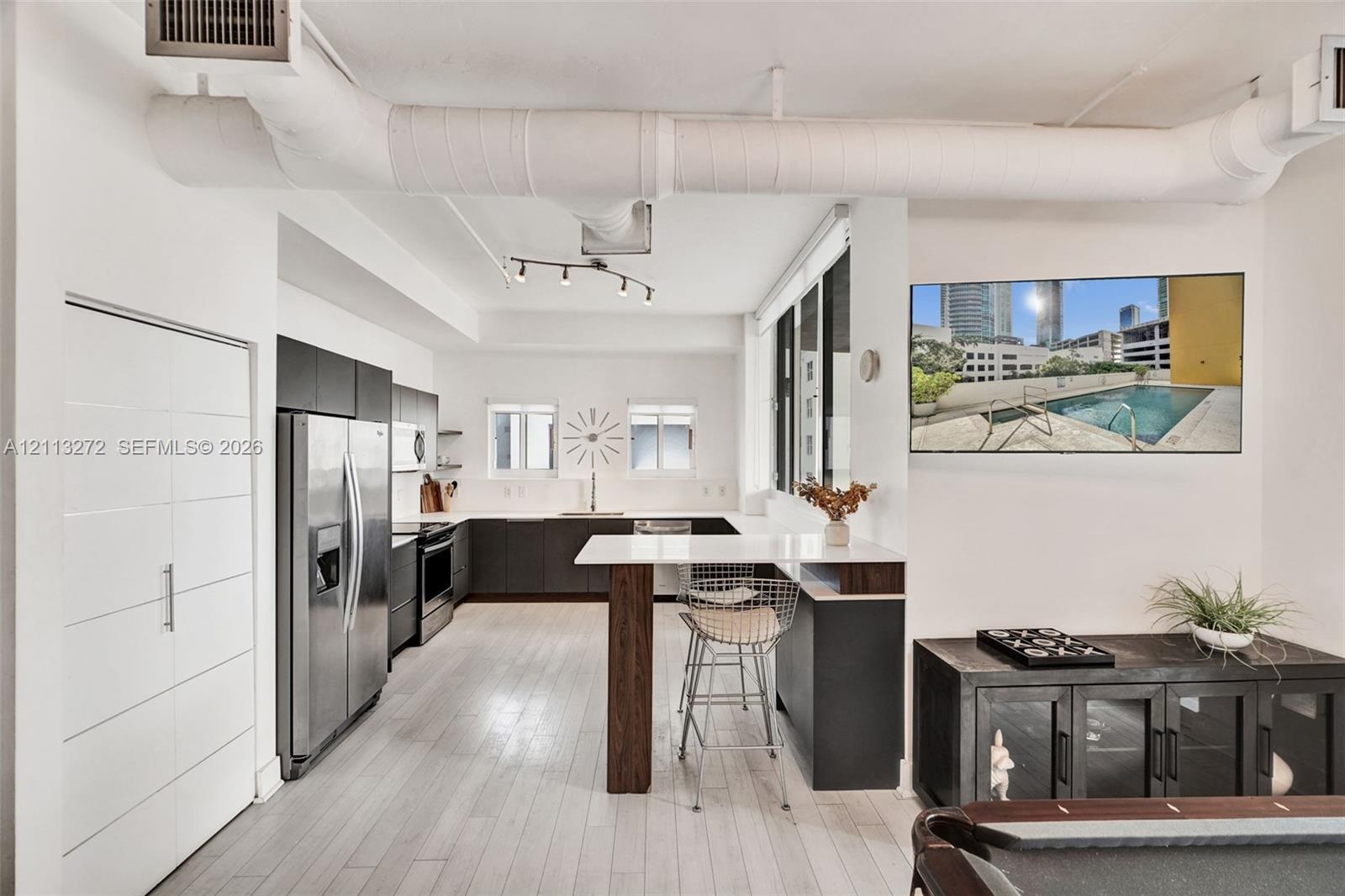 Kitchen featuring dark cabinetry, stainless steel appliances, white countertops, a breakfast bar, and wood-finish flooring