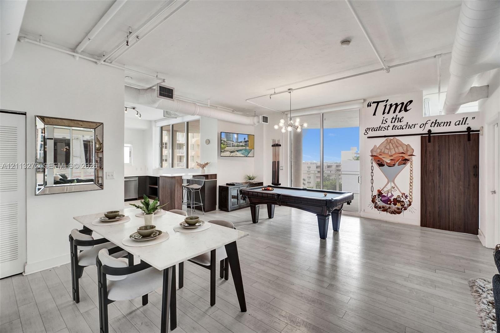 Open-concept interior featuring light wood-finish flooring, exposed industrial-style ceiling ductwork, floor-to-ceiling windows, and a dark wood barn-