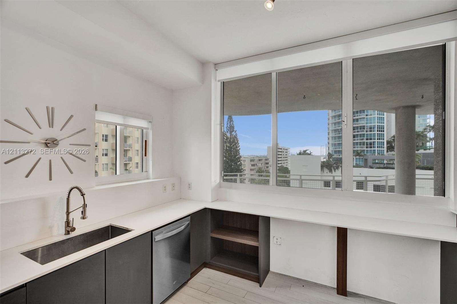 Kitchen featuring expansive window walls, stainless steel undermount sink with gooseneck faucet, integrated dishwasher, dark cabinetry with flat-panel