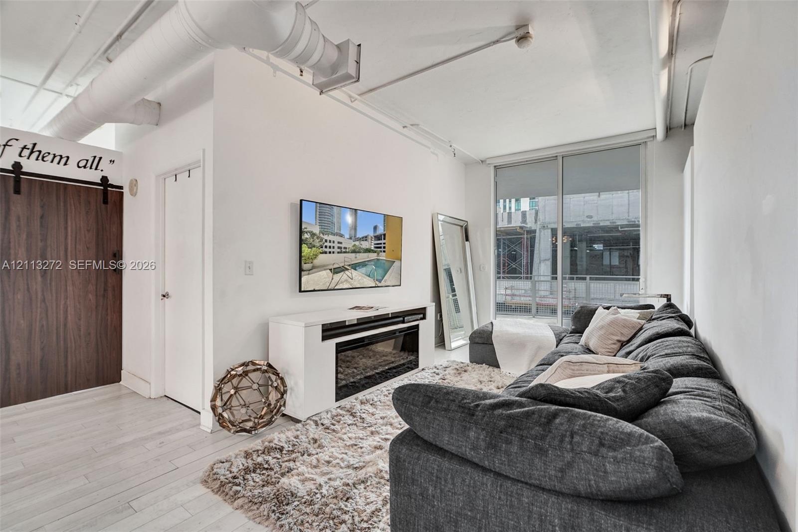Industrial-style interior featuring exposed overhead ductwork, wood-finish sliding barn door, wood-finish flooring, and a glass sliding door providing