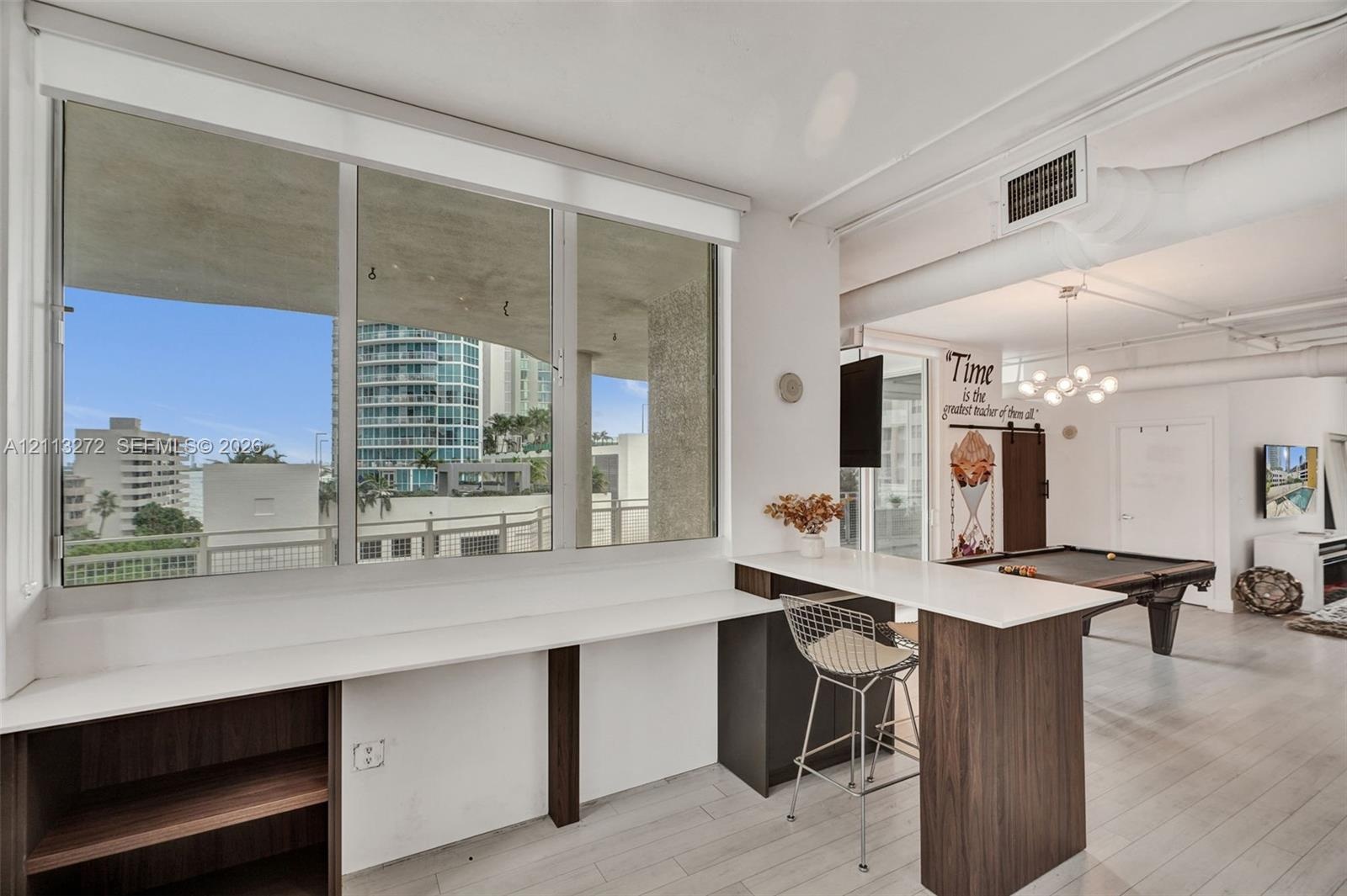 Built-in desk with quartz countertop and wood-finish cabinetry, floor-to-ceiling windows, light-toned tile flooring, exposed ceiling ductwork, and mul
