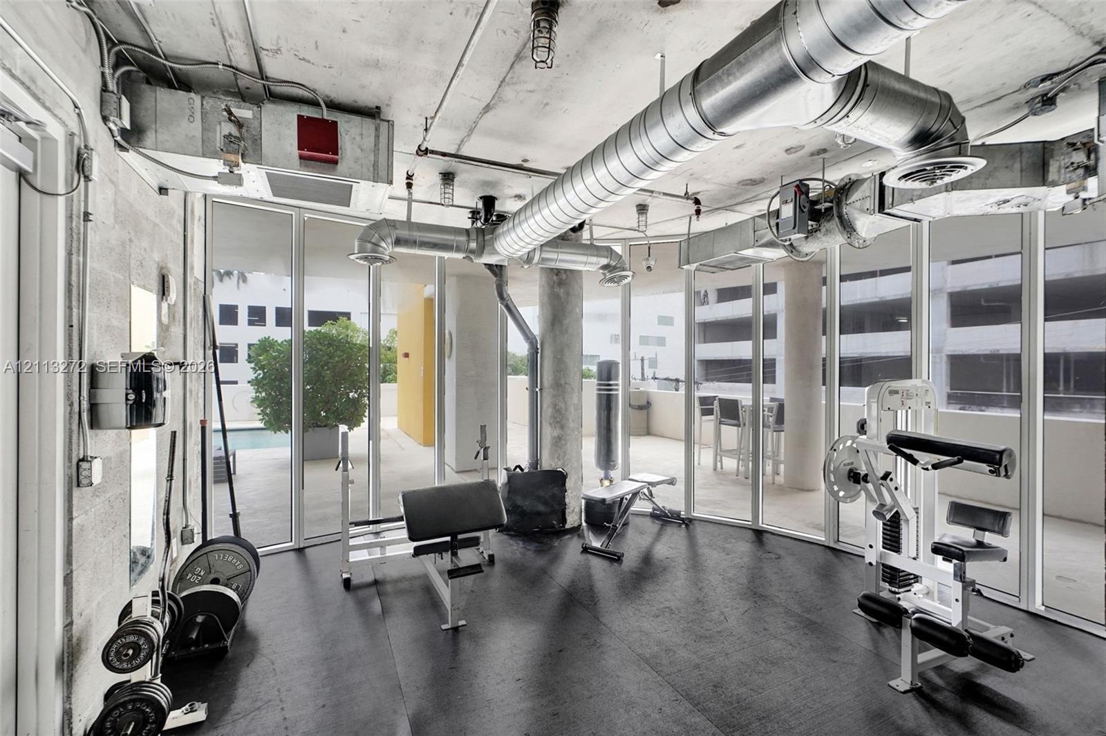 Industrial-style interior featuring exposed concrete ceilings, metallic ductwork, floor-to-ceiling glass wall panels, and impact-resistant rubber floo