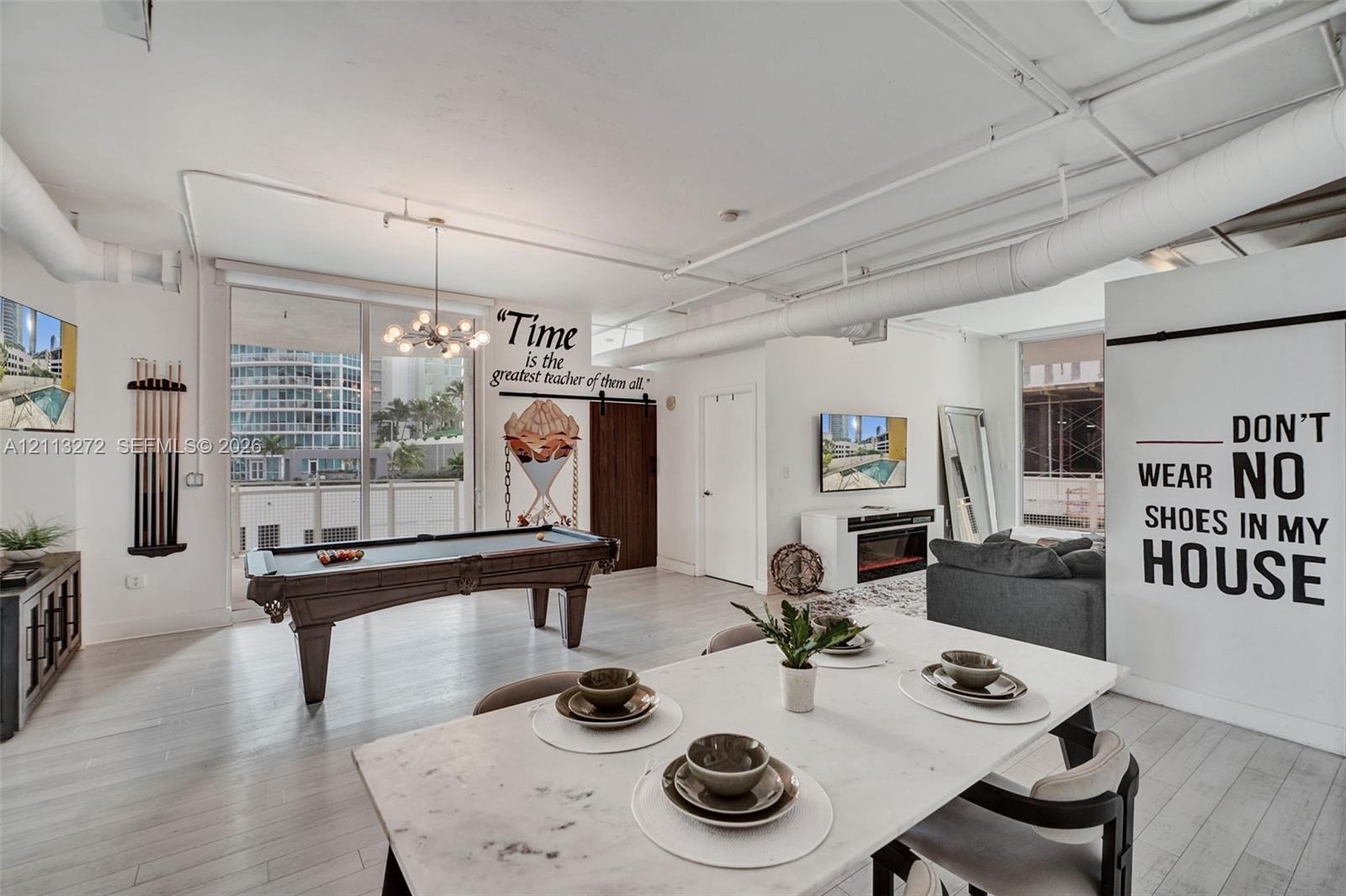 Open-concept living space featuring high ceilings with exposed ductwork, wood-finish flooring, floor-to-ceiling glass sliding doors, and a rustic slid