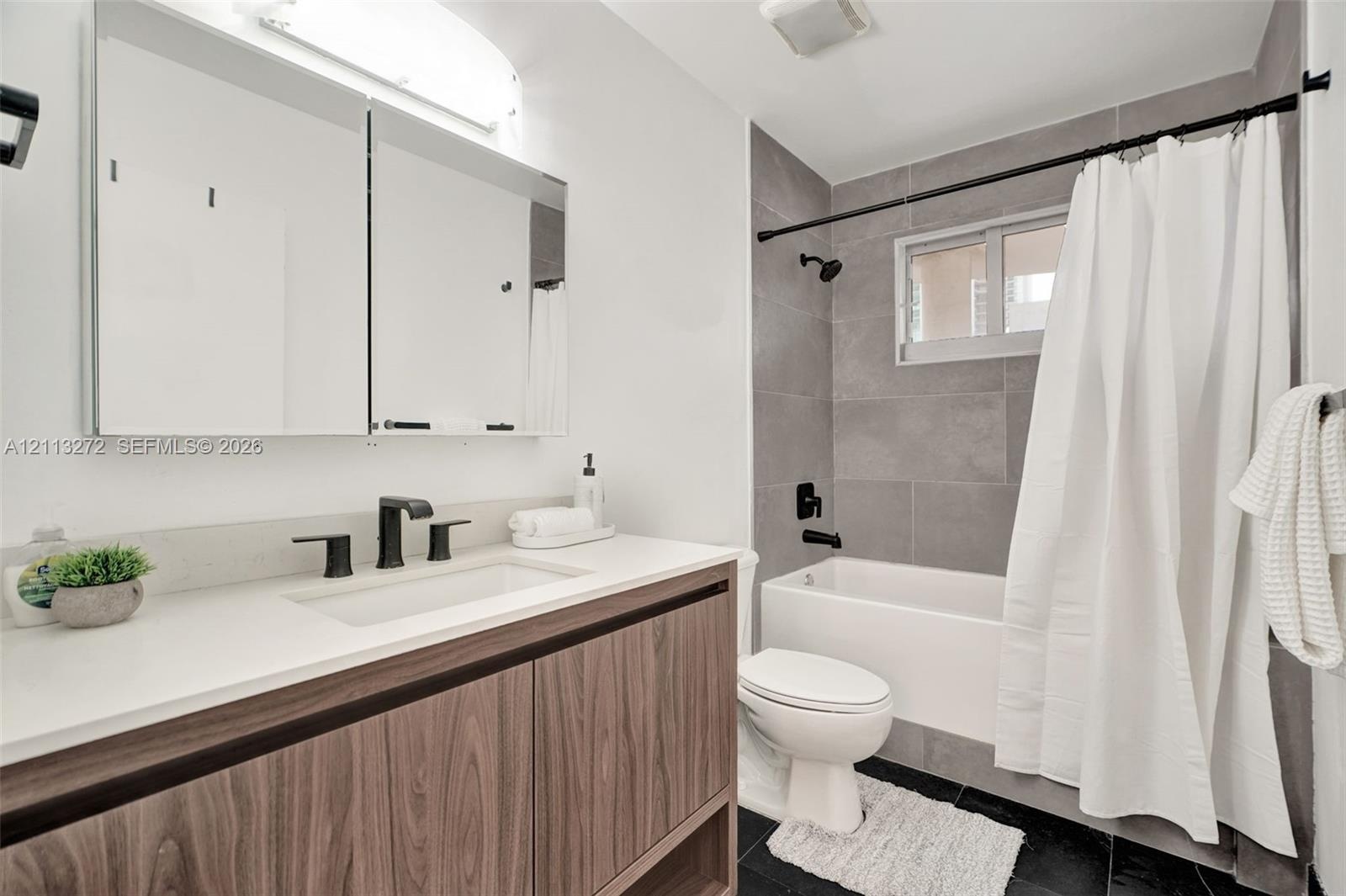 Bathroom featuring a wood-finish vanity with a white countertop, large mirrored medicine cabinet, matte black plumbing fixtures, and a tub-shower comb