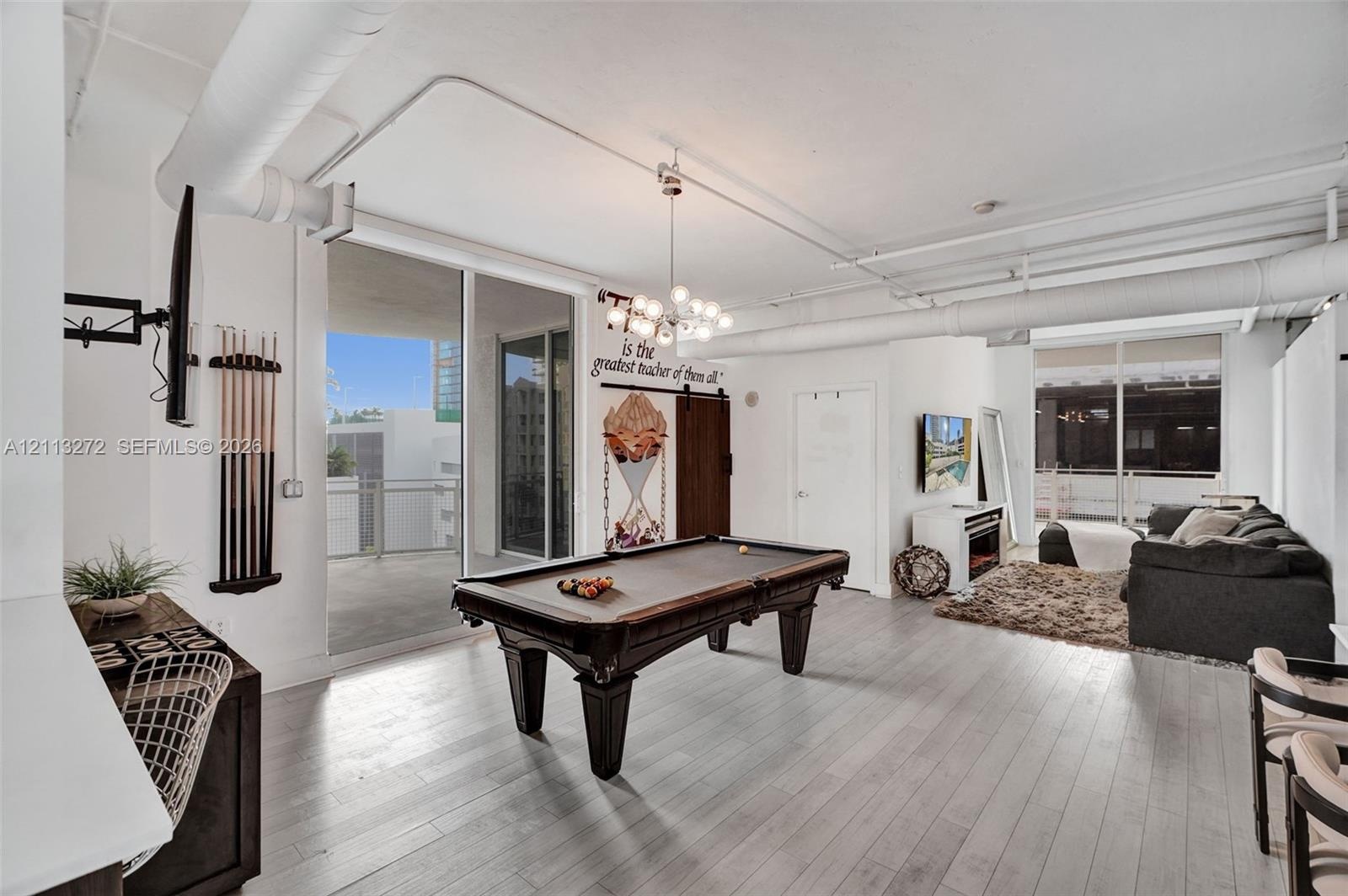 Open-concept industrial-style interior featuring high ceilings with exposed ductwork, wood-finish flooring, a multi-globe chandelier, and sliding glas