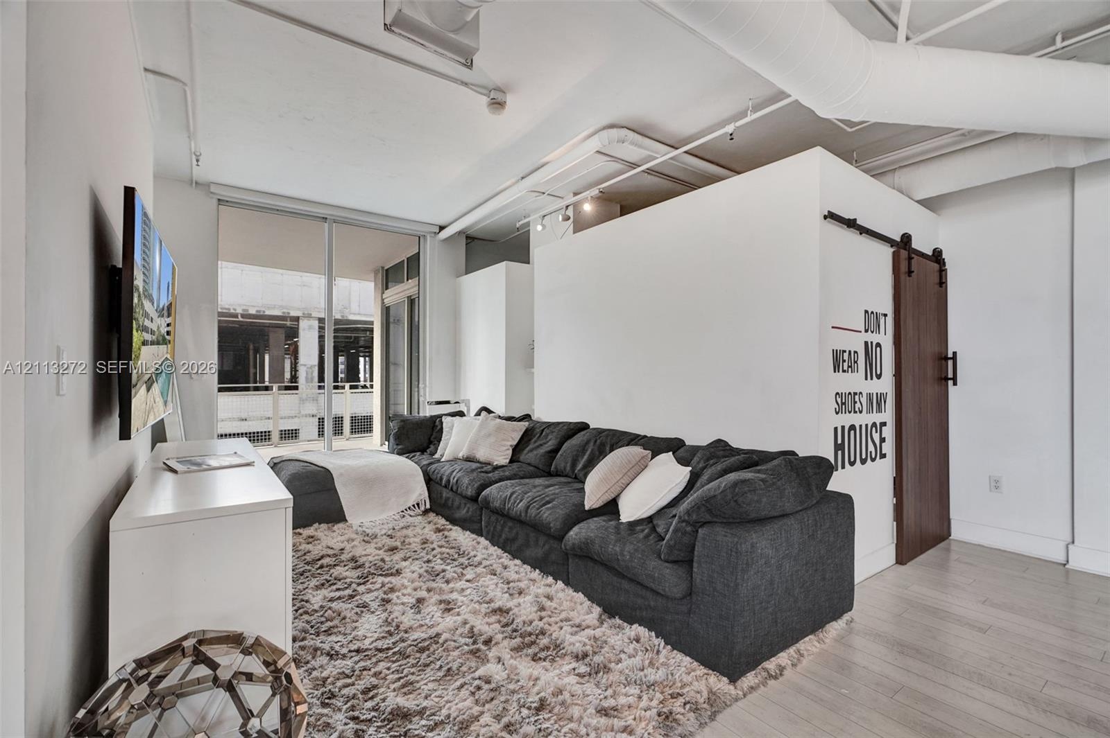 Industrial-style interior featuring high ceilings with exposed ductwork, wood-finish flooring, and a sliding barn door with matte black hardware