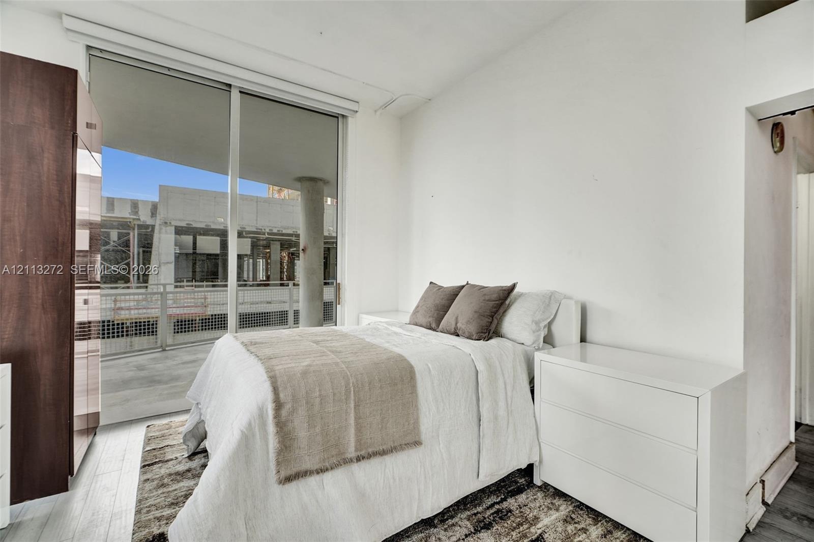 Floor-to-ceiling sliding glass door, private balcony, wood-finish flooring, and integrated full-height storage cabinetry