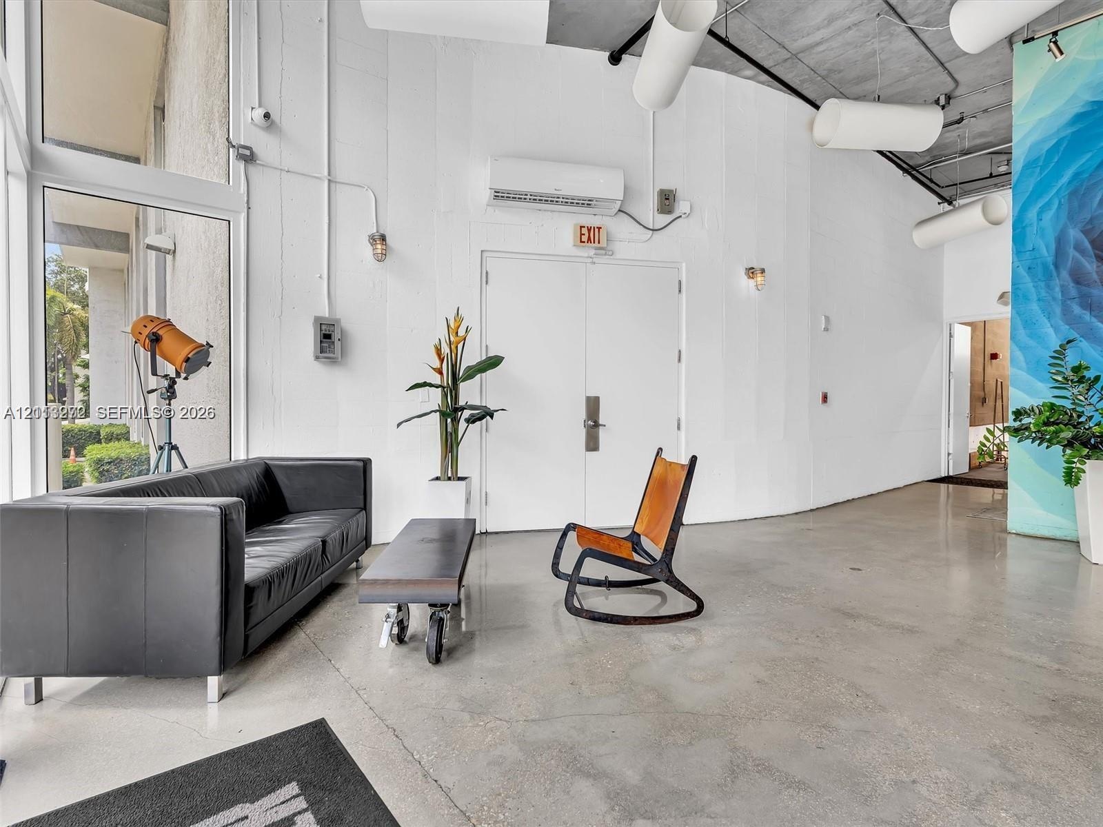 Industrial-style interior featuring polished concrete flooring, exposed ceiling with cylindrical ductwork, floor-to-ceiling windows, and a curved arch