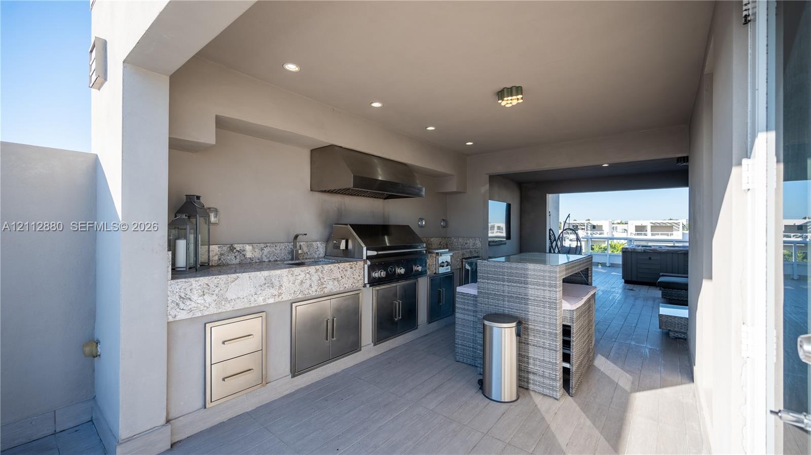 Covered outdoor kitchen featuring a built-in stainless steel grill, range hood, stone countertop with integrated sink, and stainless steel under-count